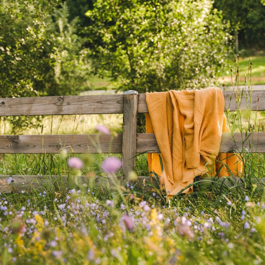 Cotton blanket hanging on a wooden fence in front of summer flower field